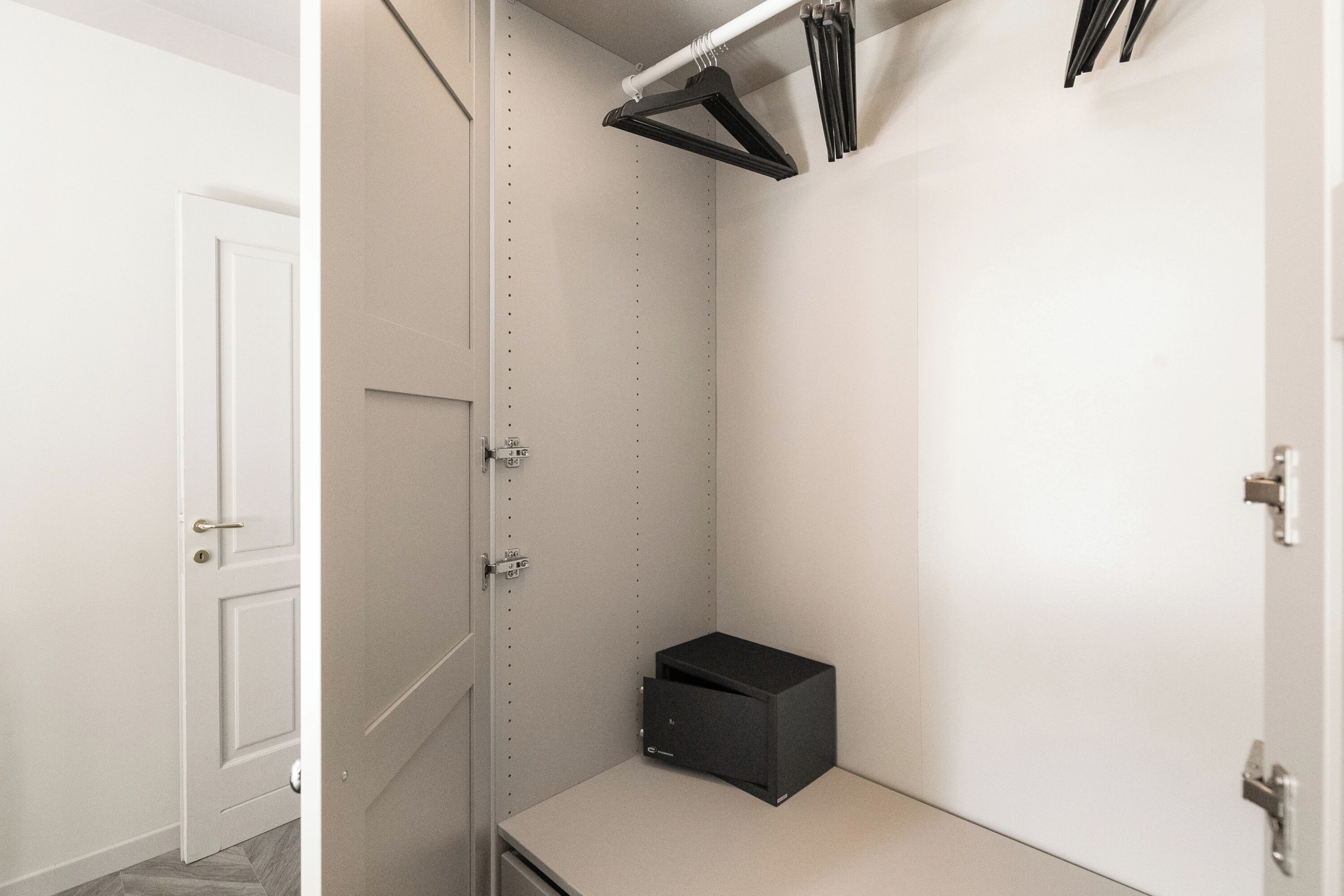 A walk-in closet with a door, a shelf, and a small black box on the floor.