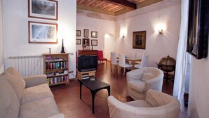 Een woonkamer met een open haard, een televisie en een eethoek met stoelen en een tafel.