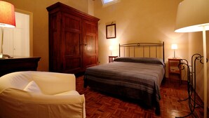 Een slaapkamer met een bed, een houten garderobe, een bureau met lamp en een stoel.