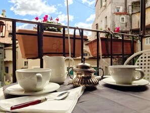 A table with two white cups and a silver teapot on a balcony with a view of buildings and flowers. - Wonderful Apartment With Balcony In Piazza Margana (Rome)