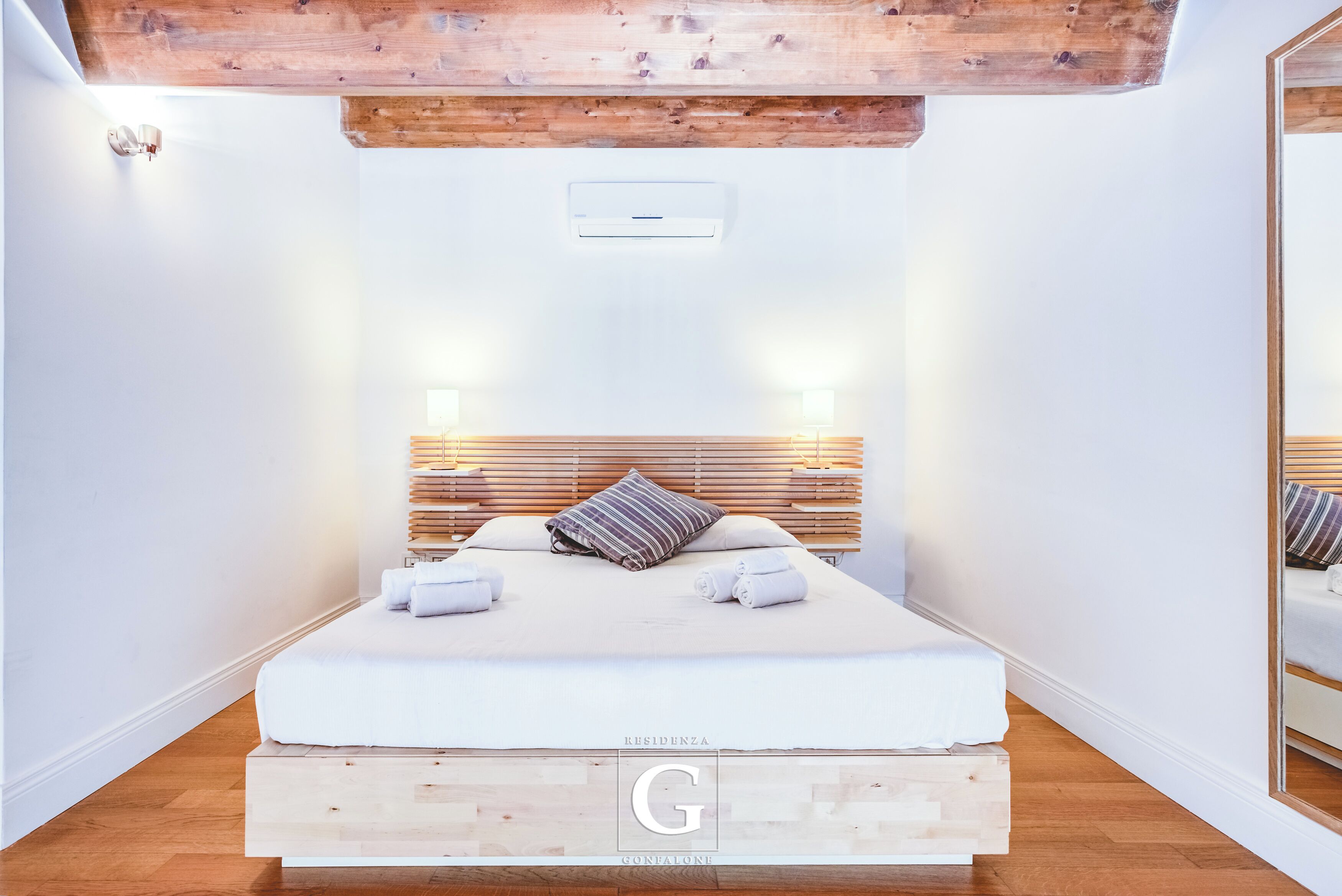 Une chambre à coucher moderne avec une tête de lit en bois, un lit recouvert de draps blancs et deux lampes de chevet.