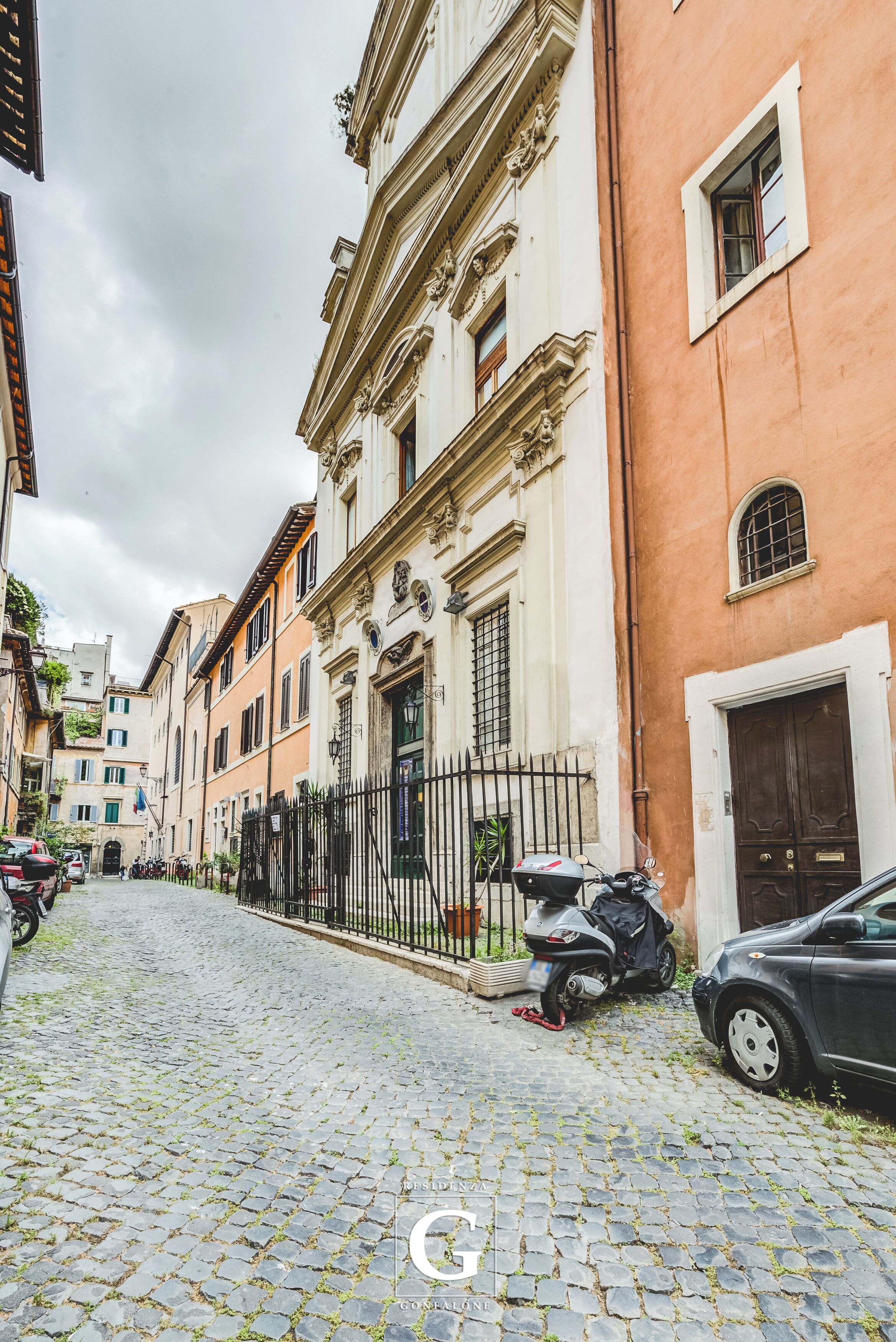 A cobblestone street lined with historic buildings, a parked scooter, and a car.