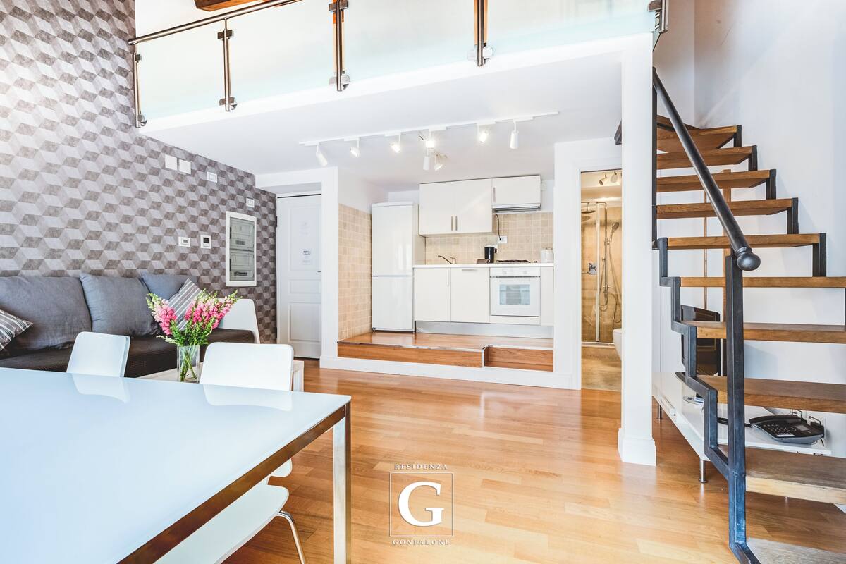 A spacious living area with a dining table, sofa, and kitchen in the background.