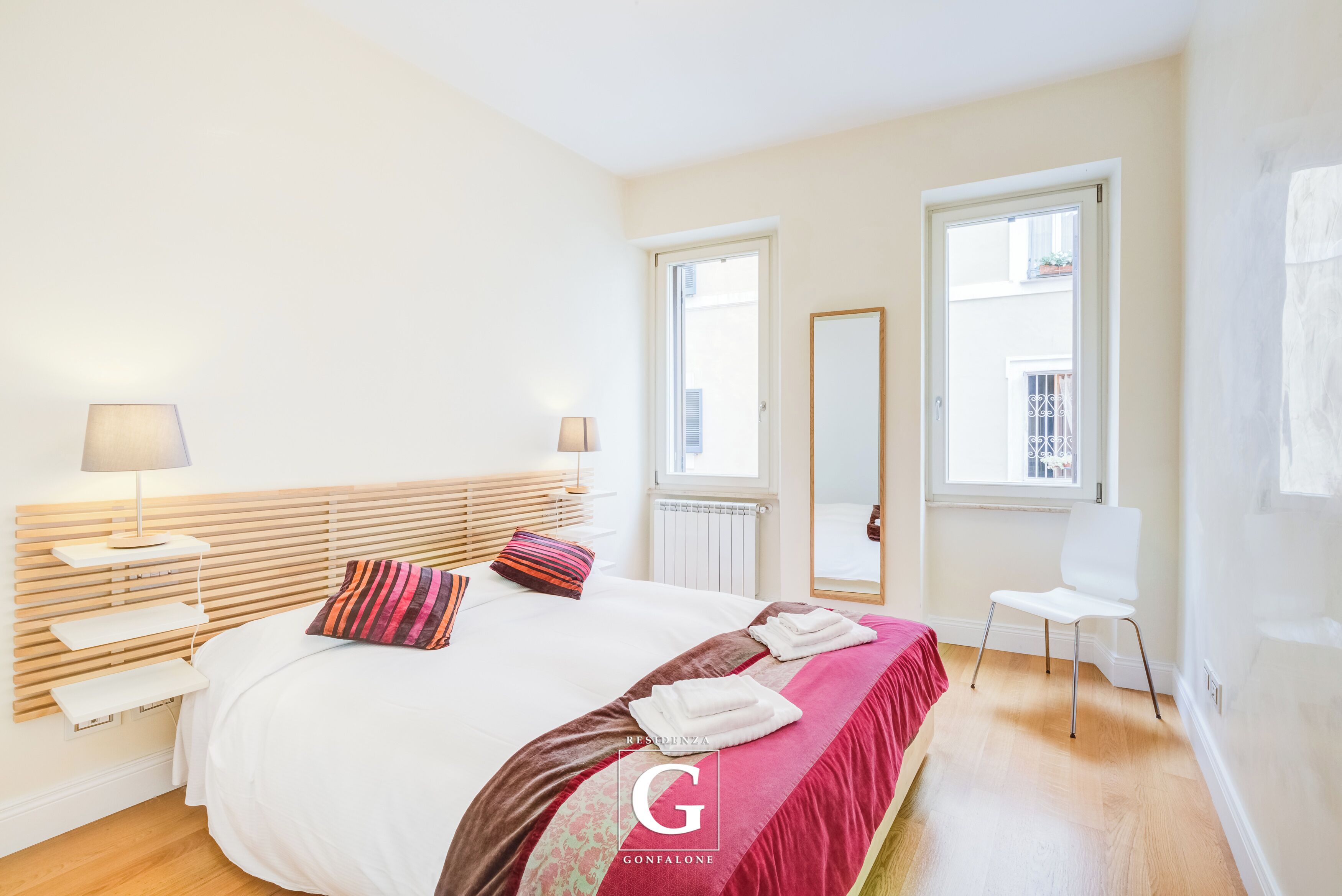 Une chambre à coucher avec un lit, des lampes de chevet, une chaise et une fenêtre.