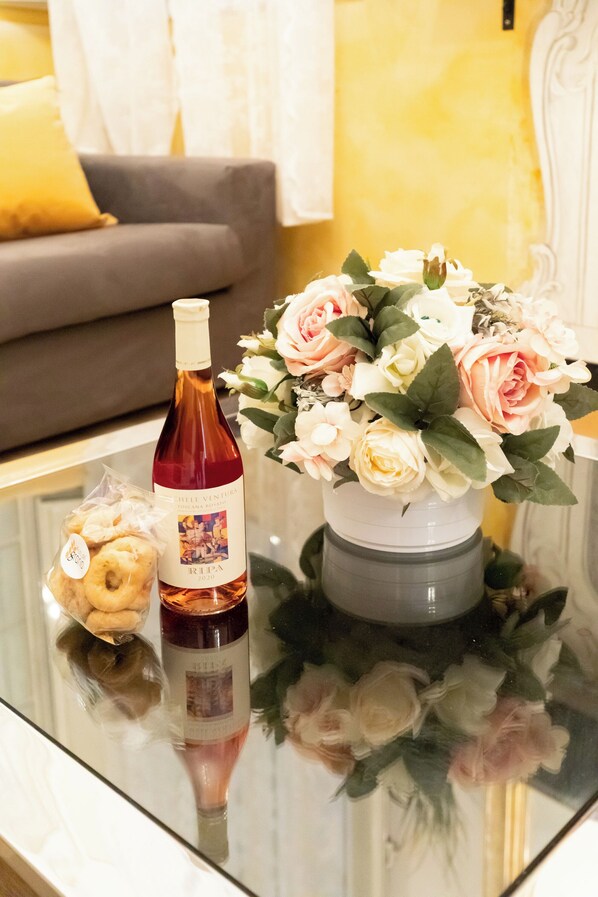 A glass table with a bottle of wine, a bouquet of flowers, and a bag of snacks. - Via Dei Banchi Vecchi Apartments (Rome)