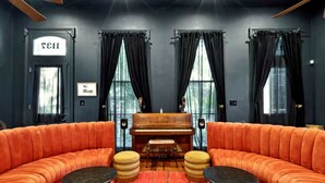 A room with a grand piano, a curved orange sofa, and two ottomans. - Iconic Mansion w/Private Pool & Spa, Walk Downtown (New Orleans)