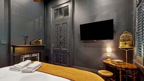 A hotel room with a bed, a television mounted on the wall, a small table with a lamp, and a decorative door. - Iconic Mansion w/Private Pool & Spa, Walk Downtown (New Orleans)