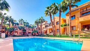 Une piscine entourée de palmiers et d’immeubles dotés de balcons.