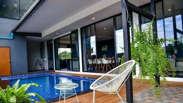 A modern outdoor pool area with a wooden deck, a white chair, and a potted plant. - Brick Box Pool Villa & Café (Doi Saket)