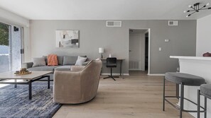 Uma sala de estar moderna com um sofá, uma mesa de centro e uma área de jantar com uma cadeira e mesa.