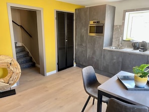 A modern kitchen with a built-in oven, a dining area with a table and chairs, and a staircase leading to a landing.