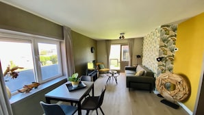 Un salon moderne avec un coin repas, de grandes fenêtres et un mur d’accent jaune.