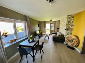 A modern living room with a dining area, large windows, and a yellow accent wall.
