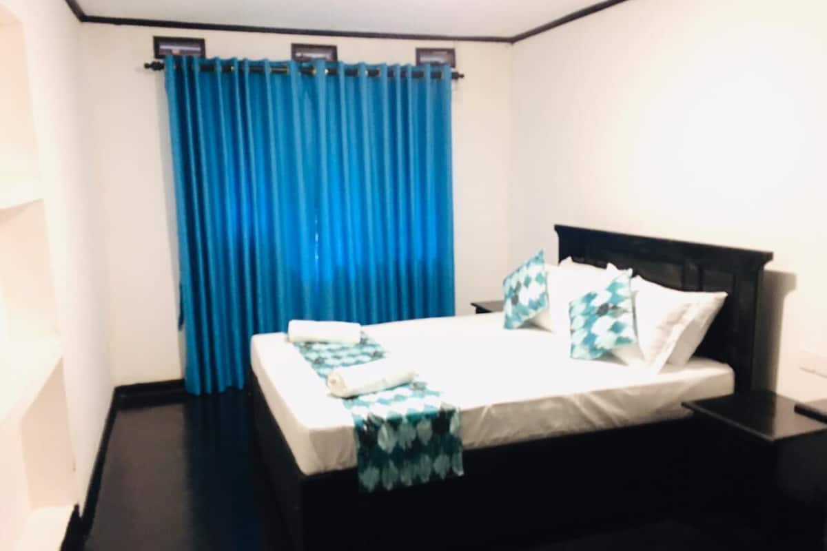 A neatly made bed with a white mattress and blue bedding, a black headboard, and a blue curtain.