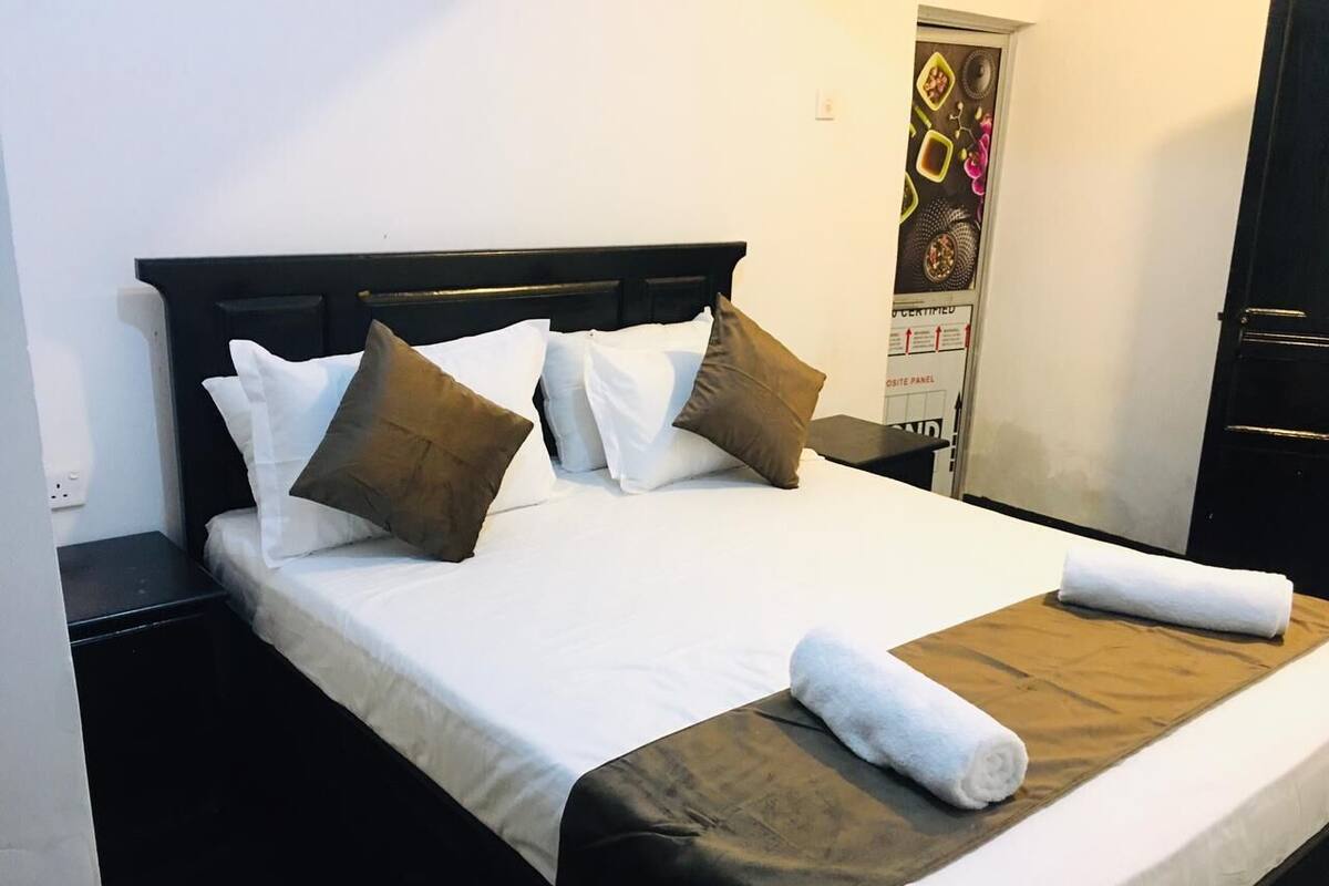 A neatly made bed with white and brown bedding, a wooden headboard, and a wooden side table.