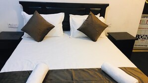 Ein ordentlich bezogenes Bett mit weißen und braunen Kissen, einer schwarzen Tagesdecke und zwei aufgerollten weißen Handtüchern.