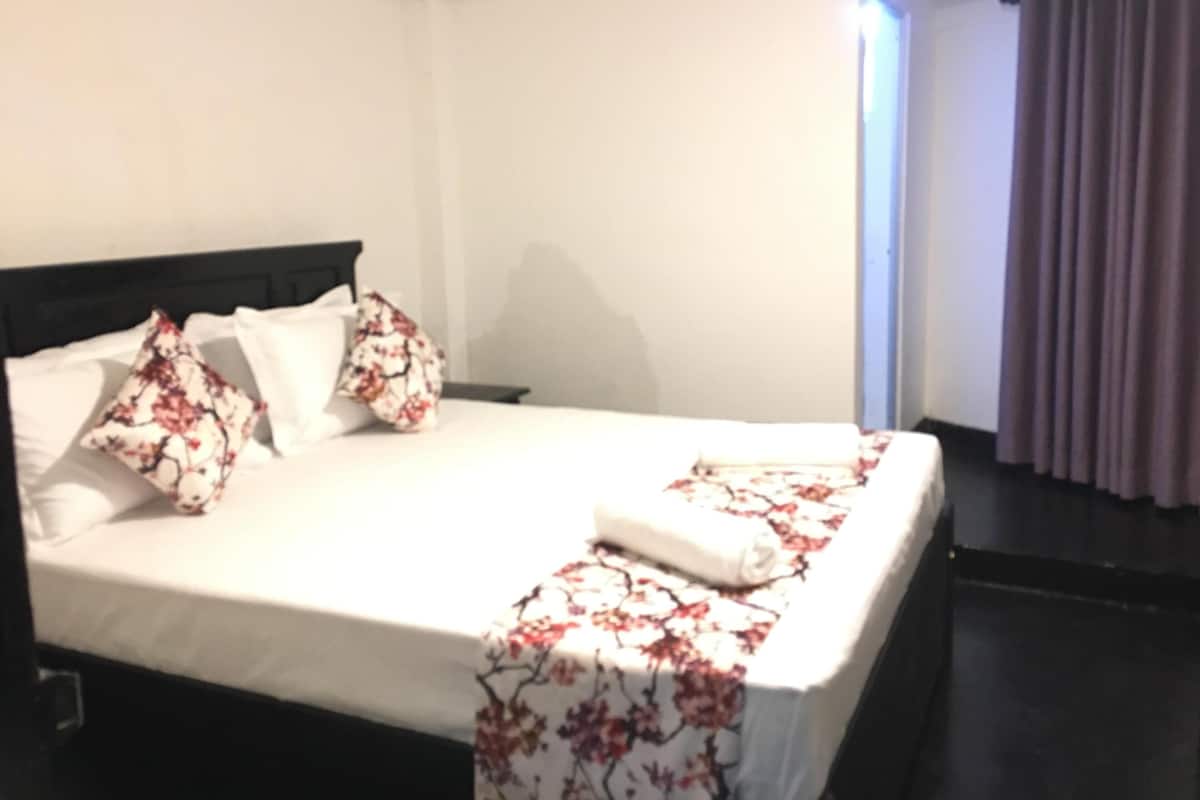 A hotel room with a neatly made bed, a black headboard, and a window with curtains.