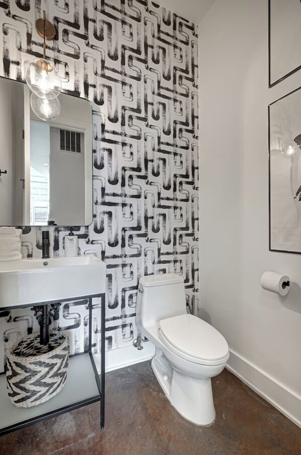 A bathroom with a black and white geometric patterned wallpaper, a white toilet, a white sink with a black faucet, and a round mirror above the sink.