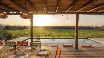 Uma área de refeições com vista para um campo, uma piscina e uma estrutura de pérgola.