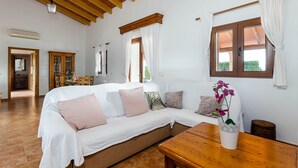 Ein Zimmer mit einer Couch, einem Holztisch, einem Fenster mit Vorhängen und einer Holzbalkendecke.