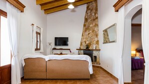 Ein Schlafzimmer mit Bett, Fernseher, einem Kamin aus Stein und Blick auf einen anderen Raum.