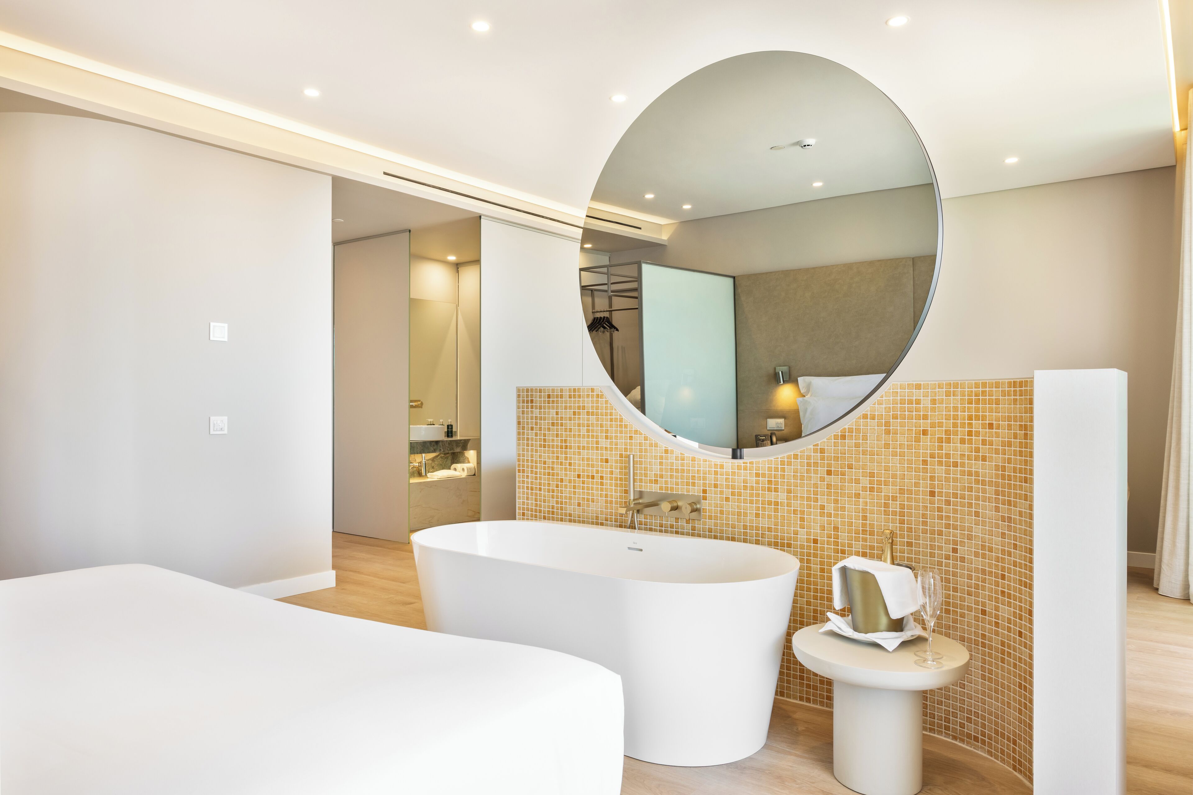A modern bathroom with a freestanding bathtub, a round mirror, and a small vanity table.