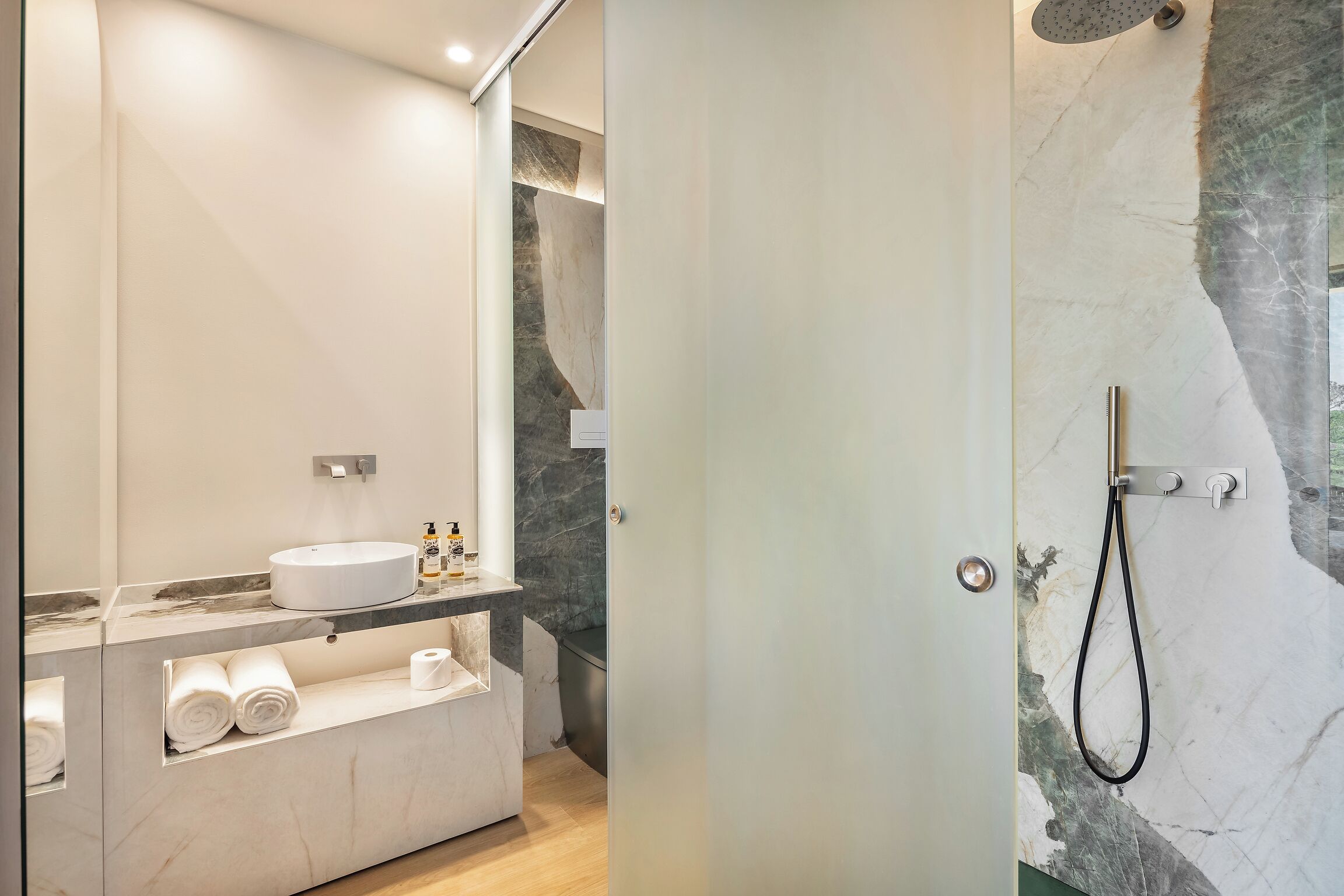 Un baño moderno con lavamanos de mármol, espacio para toallas y ducha con cabezal de mano.
