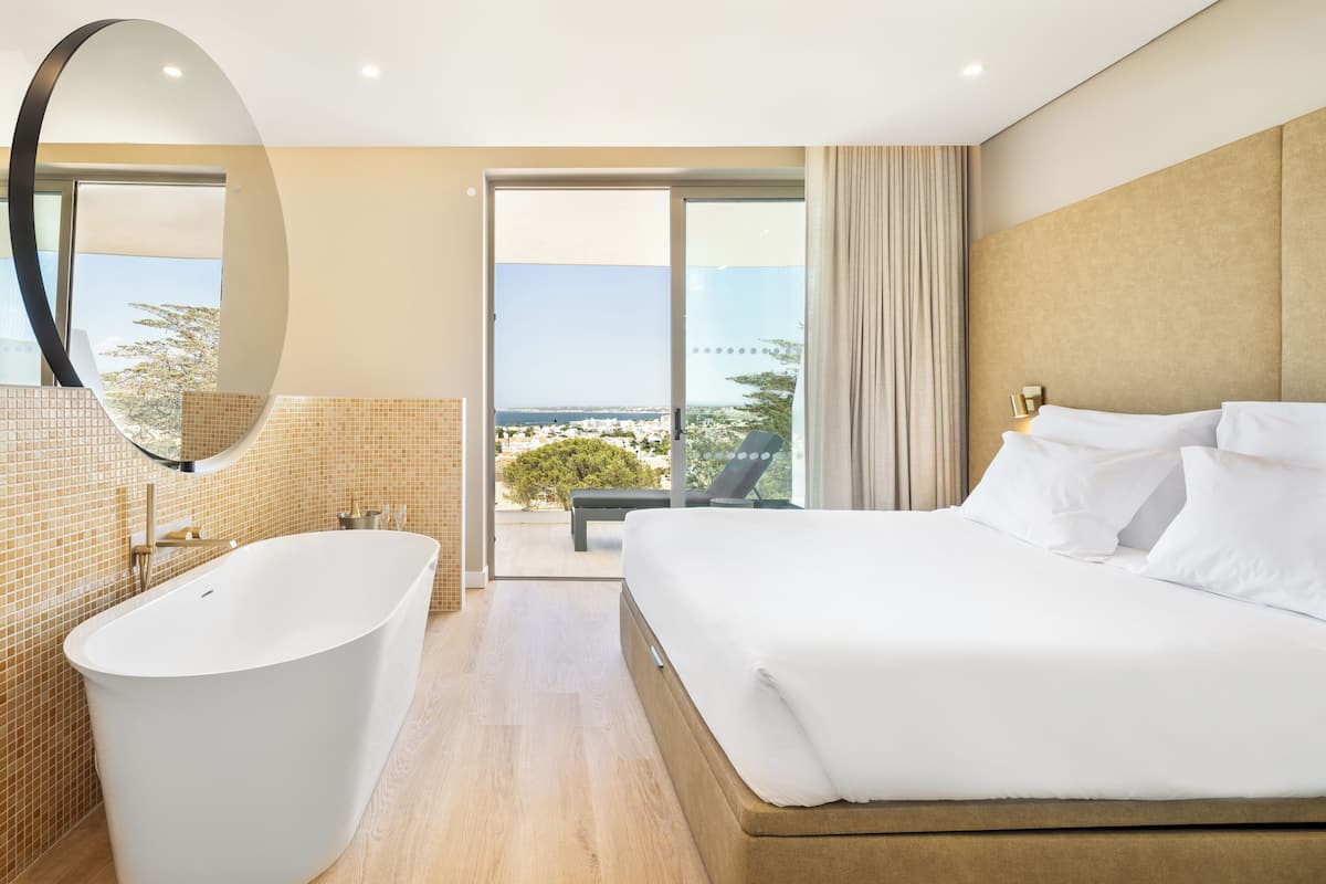 A modern hotel room with a large bed, a bathtub, and a balcony with a city view.