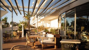 An outdoor patio with wicker furniture, a wooden deck, and a glass enclosure. - Castelo Suites Hotel (Albufeira)