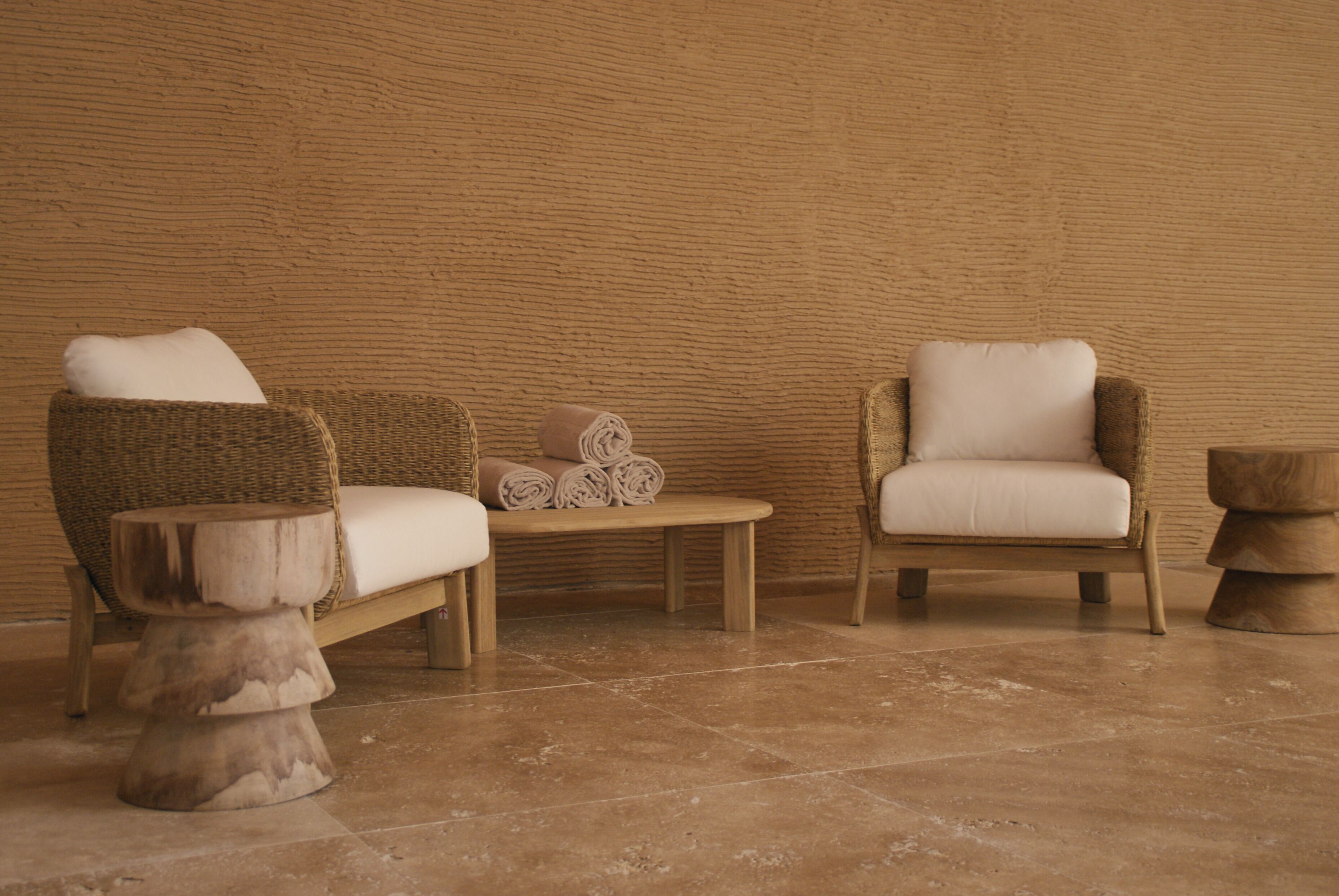 Una habitación con dos sillones de mimbre, una mesita de madera y un taburete de madera.