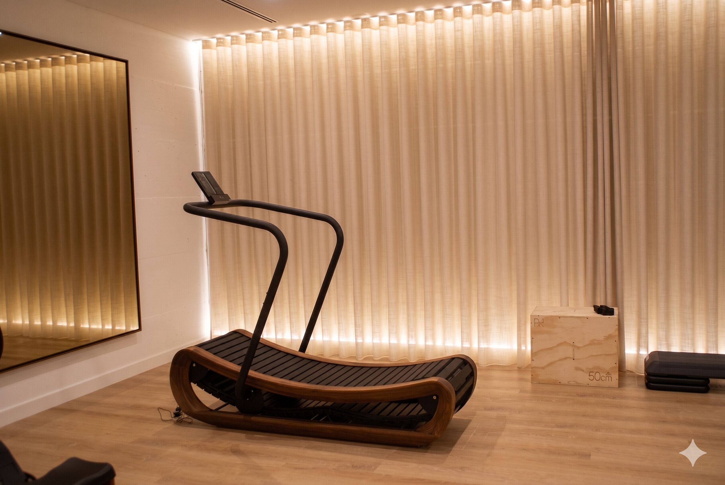 A modern room with a wooden floor, a treadmill, a small wooden box, and a mirror on the wall.