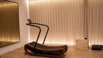 A modern room with a wooden floor, a treadmill, a small wooden box, and a mirror on the wall.