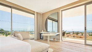A modern hotel room with a large bed, a round table, and a view of the city and sea. - Castelo Suites Hotel (Albufeira)