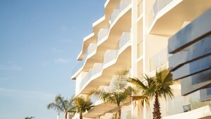 A modern hotel with a unique architectural design featuring curved balconies and large windows. Palm trees are visible in front of the building. - Castelo Suites Hotel (Albufeira)