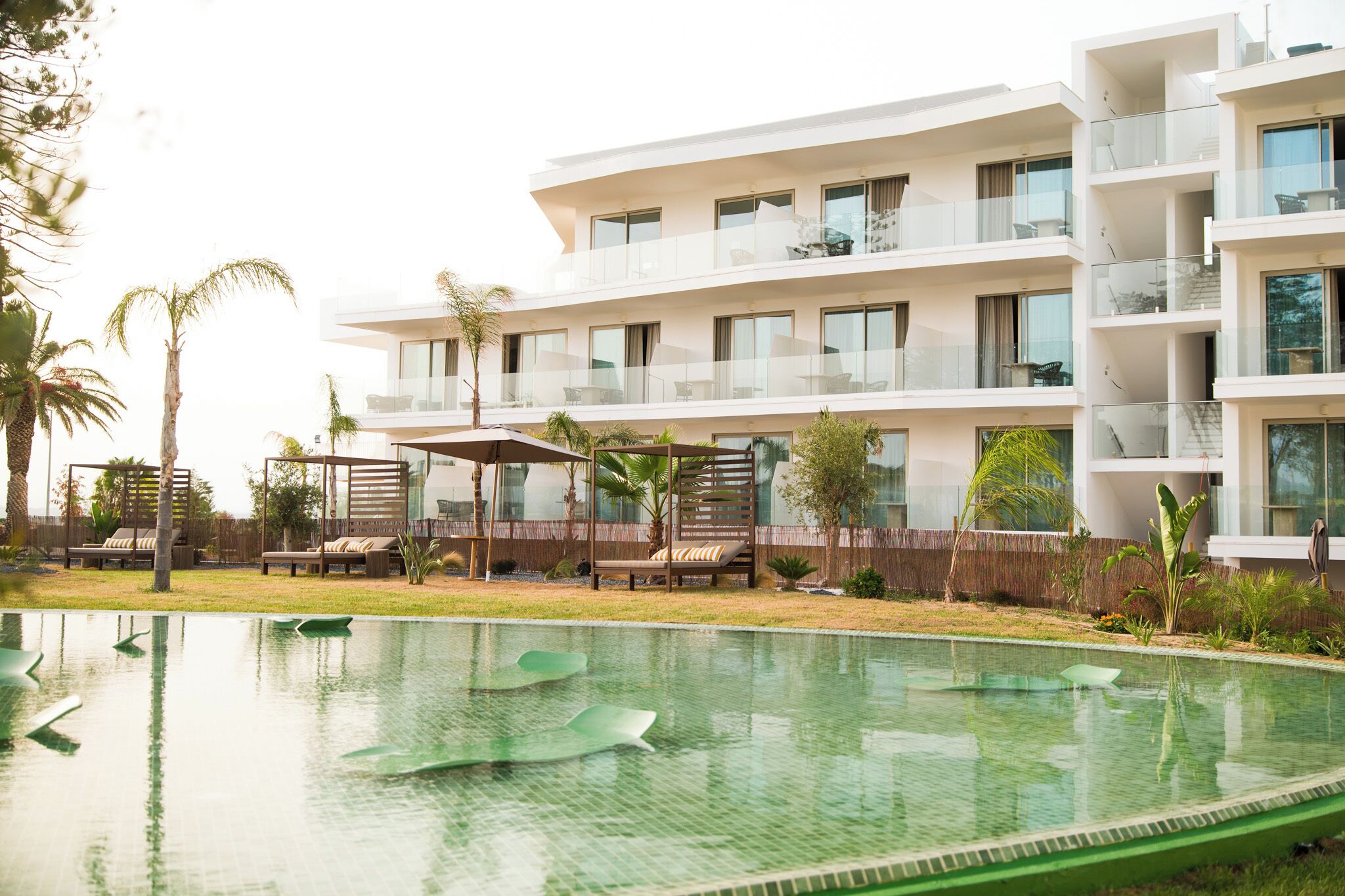 Un hotel moderno con piscina, mobiliario exterior y un jardín exuberante.