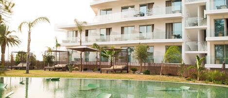Un hotel moderno con piscina, mobiliario exterior y un jardín exuberante.