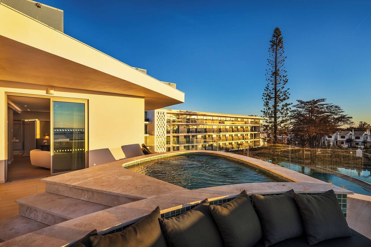 A modern hotel with a swimming pool, outdoor seating, and a view of other buildings.
