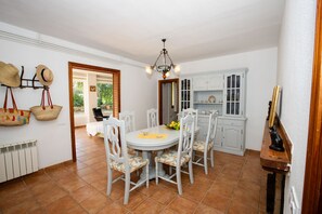 Un espace repas avec une table ronde, des chaises blanches, un lustre et une vue sur l’extérieur.