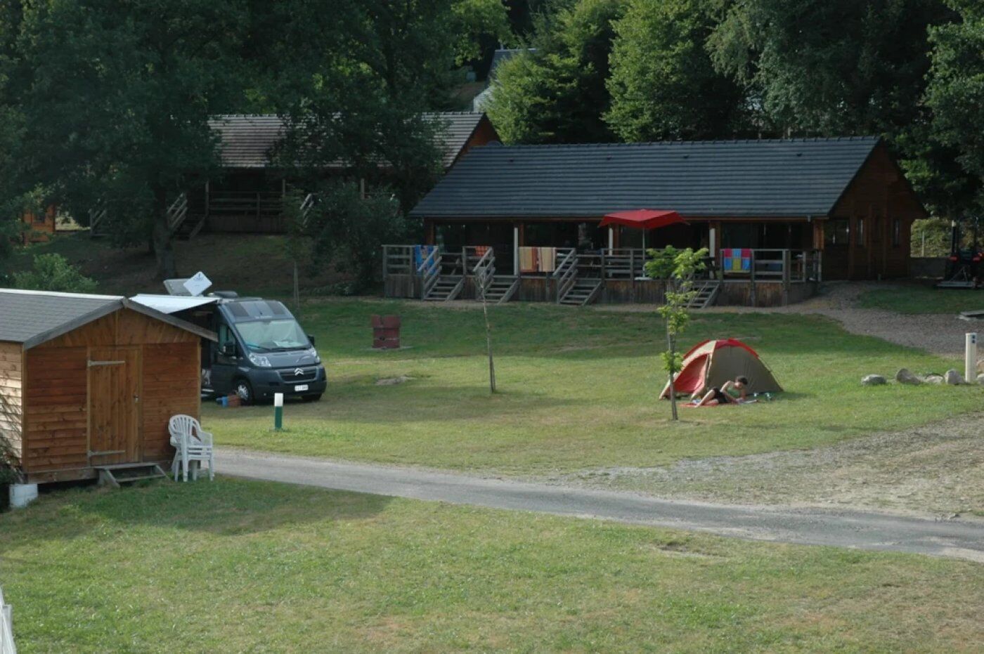 Ein Campingplatz mit Zelt, einer kleinen Holzhütte und einem größeren Gebäude mit rotem Sonnenschirm.