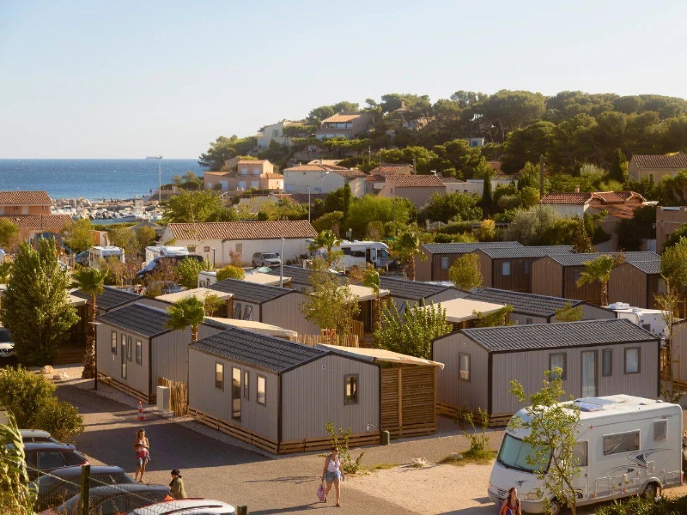 A caravan park with multiple caravans and mobile homes, a beach in the background, and a hilly landscape.