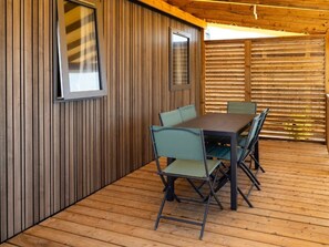 Une terrasse en bois avec une table et des chaises, une fenêtre et un mur avec des lattes verticales.