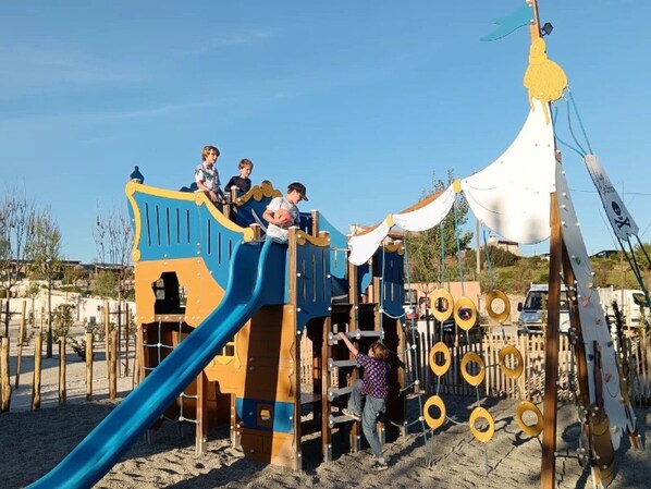 A playground with a slide, climbing structures, and a tent-like structure with ropes.
