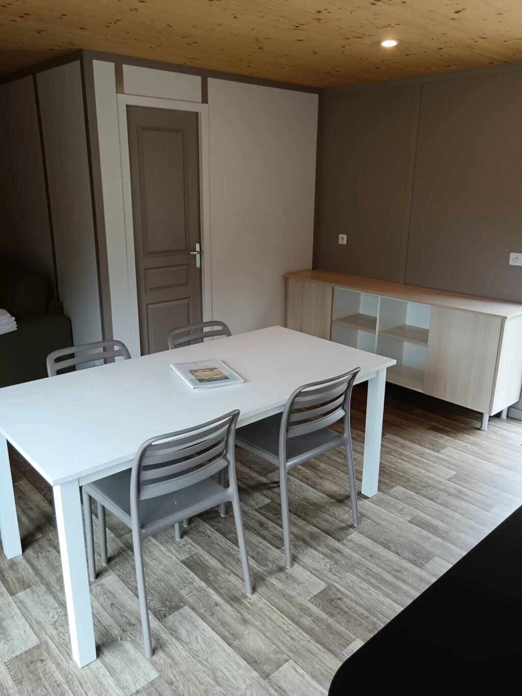 Une cuisine de taille réduite avec une table et des chaises blanches, un meuble en bois et une porte.