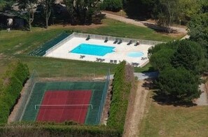 Vue aérienne d’une propriété dotée d’une piscine, d’un court de tennis et d’une zone délimitée par une clôture.