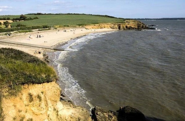 A coastal beach with a sandy shore, grassy dunes, and a rocky outcrop.