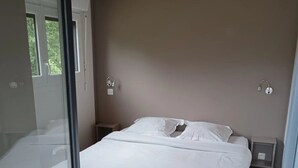 A bedroom with a bed, a nightstand, a wall-mounted light, and a window.