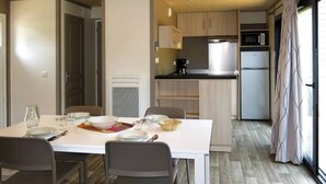 A compact kitchen with modern appliances, a dining area with a white table and chairs, and a view through a glass door.