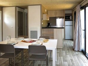 A compact kitchen with modern appliances, a dining area with a white table and chairs, and a view through a large window.