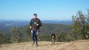 Une personne se tient sur une colline, accompagnée d’un chien, et contemple un paysage montagneux.