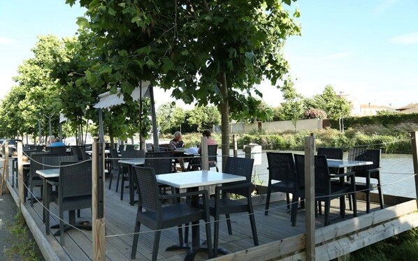 An outdoor dining area with tables and chairs, surrounded by trees and a body of water.